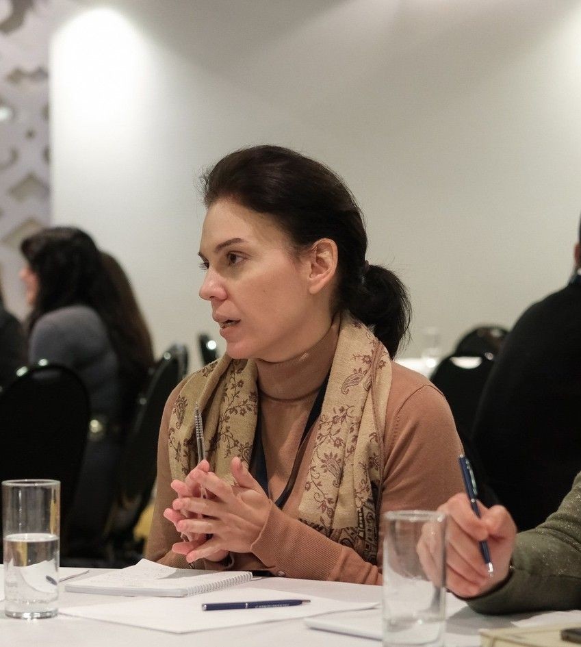 Woman with a scarf discussing at a table with notebooks and water glasses.