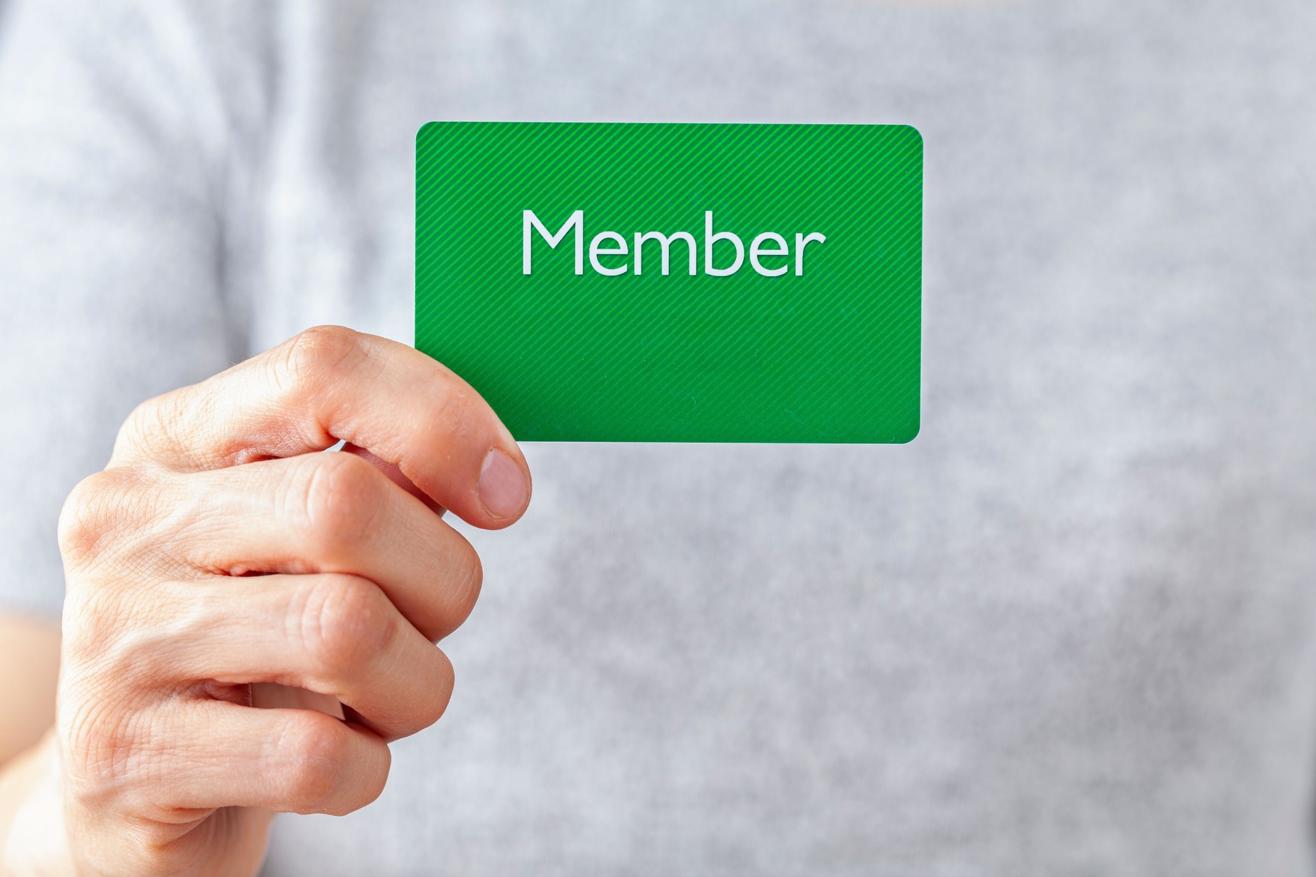 A young caucasian woman is holding a green card that says member on it